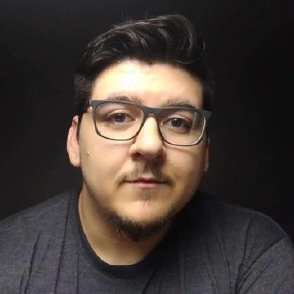 A man with short black hair and glasses looks directly into the camera.